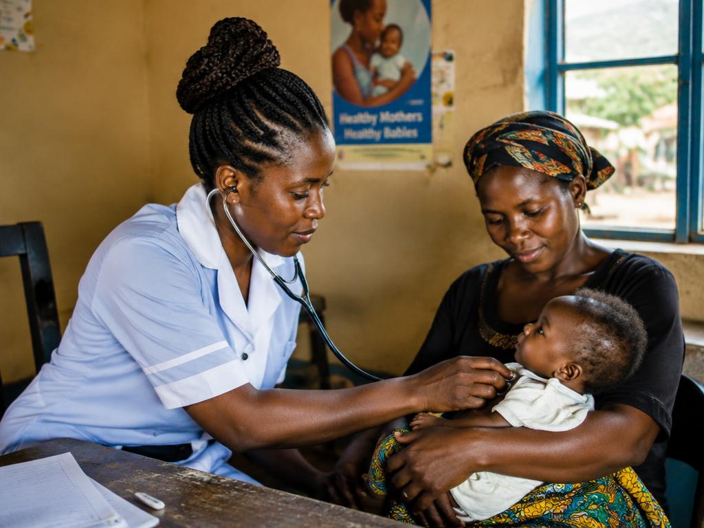 A community health worker examining a baby held by its mother
